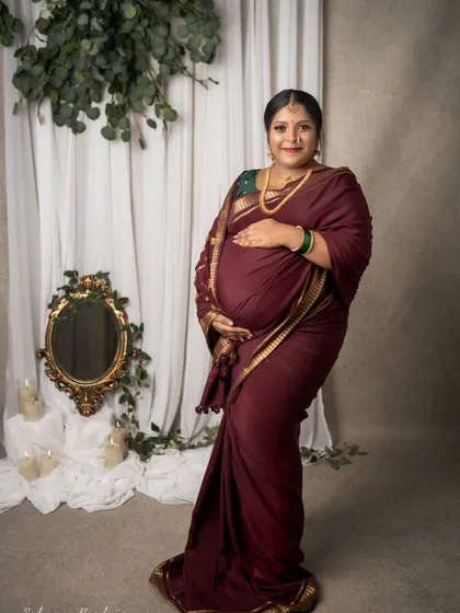 A full-length portrait showcasing the elegance of a traditional saree drape on a mom-to-be. The rich color and gold border of the saree create a truly regal look.