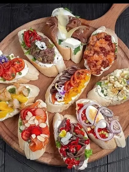 A wooden board laden with a variety of bruschetta and crostini. Toppings range from classic tomato and basil to more gourmet options with fruit, cheese, and cured meats.