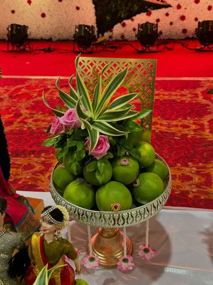 A beautiful arrangement of sweet limes in a silver pedestal bowl. The platter is decorated with fresh flowers and leaves, adding a touch of nature to the display.