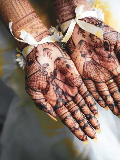 A close-up of the bride's hands, adorned with elaborate mehndi designs that tell a story, including figures of the bride and groom. This highlights the personalized details of the wedding.