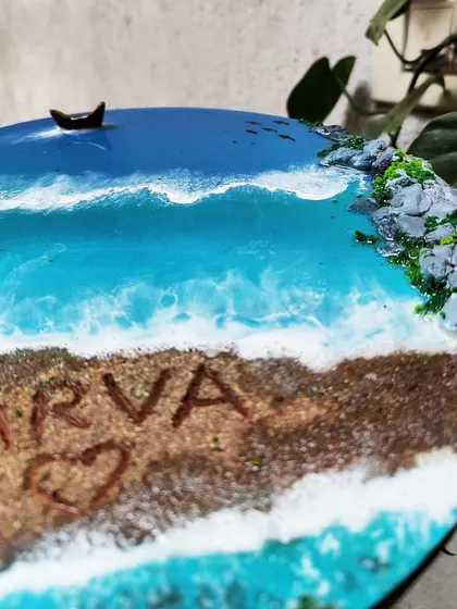 A close-up of the 'Atharva' nameplate, focusing on the name written in the sand and the texture of the waves.