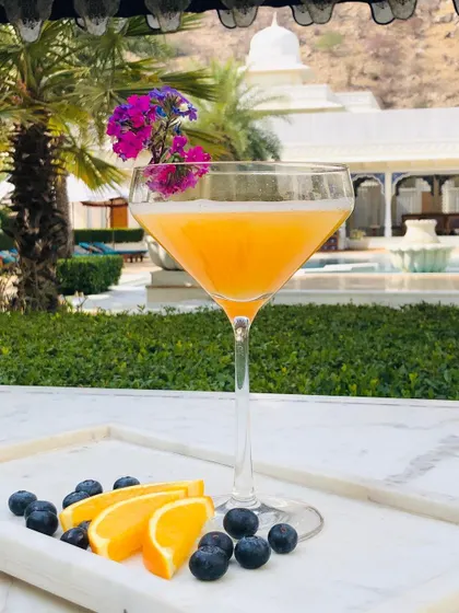 An elegant orange mocktail in a martini glass, garnished with flowers. The outdoor, resort-like setting gives this drink a luxurious, vacation feel.