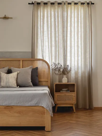A wider view of the Japandi-style master bedroom, showing the beautiful herringbone wood floors, the light-filtering jute curtains, and the overall serene and collected feel of the space.