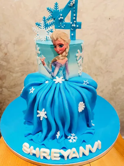 A magical two-tier Disney Frozen cake for a 4th birthday. This cake features an edible print of Elsa, whose dress is a beautifully draped fondant skirt, decorated with snowflakes.