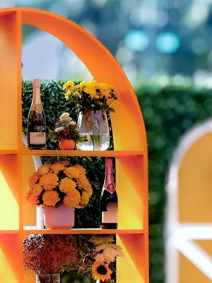 A stylish arched shelf unit used as a bar back, displaying champagne and floral arrangements that match the event's warm color palette.