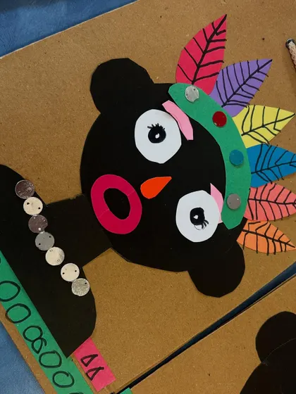 A close-up of one of the tribal art faces, showing the details of the paper feathers, sequins, and drawn patterns.