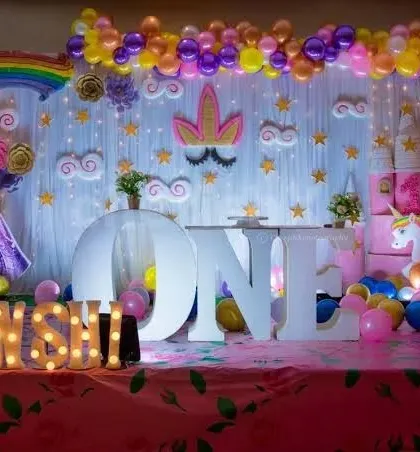 A dreamy unicorn and rainbow themed first birthday, featuring a large "ONE" marquee, unicorn figures, and a pastel rainbow balloon backdrop.