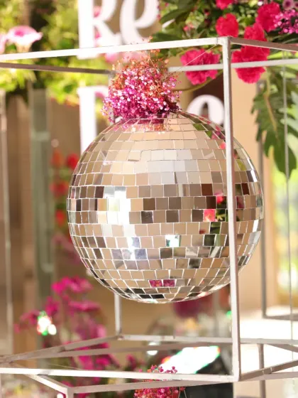 A single disco ball with a floral accent, framed within a geometric metal cube, adding a modern, artistic touch to the retro theme.