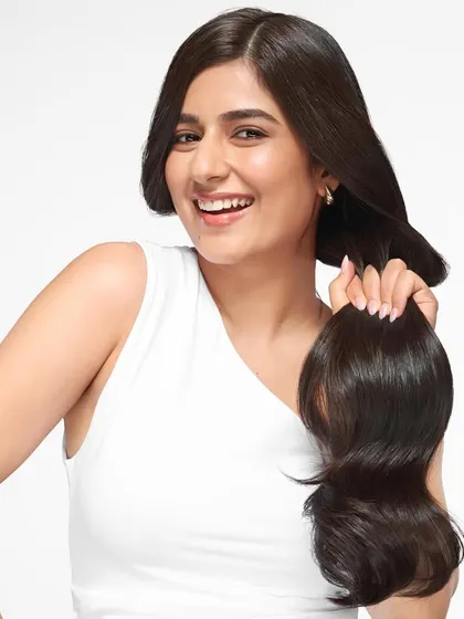 A bright and cheerful studio shot for a Dove hair campaign. The model holds a lock of her dark, healthy hair, smiling to convey confidence and satisfaction with the product's results.