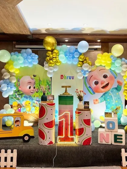 Here is a vibrant Cocomelon themed first birthday party. The setup includes large character cutouts, a custom backdrop, themed pedestals, and a light-up number '1' to bring the popular show to life.