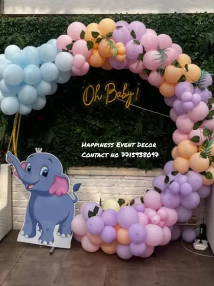 An outdoor baby shower setup with a pastel balloon ring and an 'Oh Baby!' neon sign. The cute elephant cutout adds a playful touch to the decor.