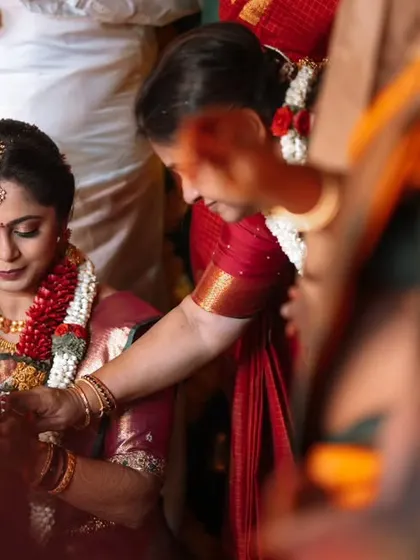 A candid shot of the bride during a puja, her hands holding a sacred coconut. The out-of-focus foreground gives a documentary feel to the image.