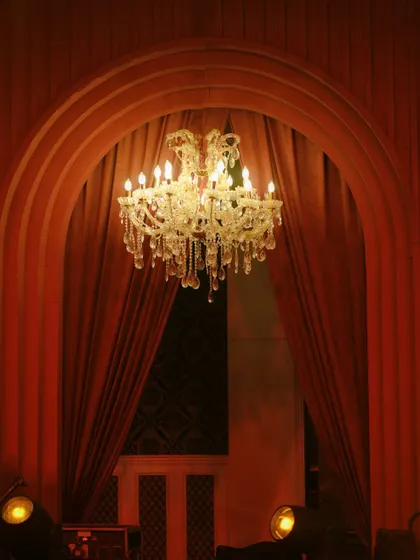 A crystal chandelier framed by an archway and heavy red drapes, creating a sense of theatrical grandeur.