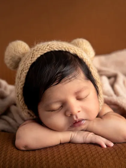 The tiny details are everything. This close-up highlights the soft cheeks, delicate lips, and peaceful expression of a sleeping newborn, complemented by a hand-knitted bear bonnet that adds a touch of cozy charm.
