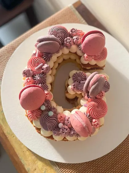 Letter cakes are a fun and personal way to celebrate. This 'G' monogram cake is decorated with beautiful monochrome buttercream swirls in shades of pink and purple, topped with matching macarons.
