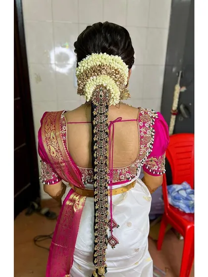 A clear view of a muhurtham braid with heavy, traditional gold jewellery pieces set against a white and pink Kanjeevaram saree. This is a classic look for a South Indian wedding.