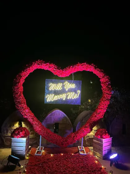 For a truly romantic gesture, we created this large heart-shaped arch from hundreds of red roses. At the center, a 'Will You Marry Me?' neon sign glows, creating a breathtaking focal point for an outdoor proposal.