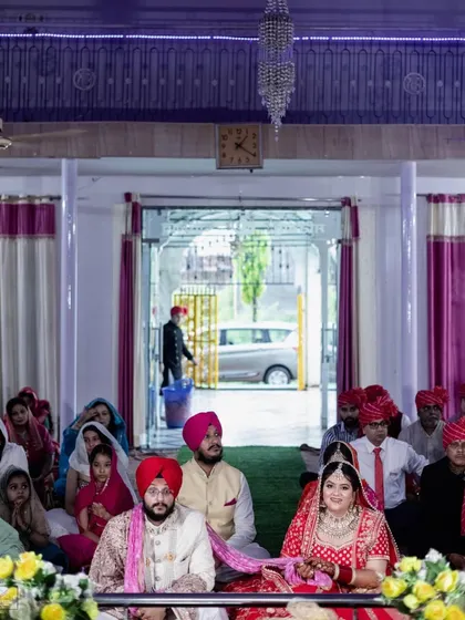 A wide-angle shot of the couple during their Anand Karaj, with all the guests seated in the background. This photo captures the sense of community and shared blessings that are part of a Gurudwara wedding.
