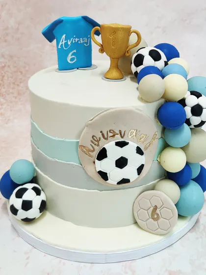 We score a goal with this stylish football champion cake. A personalized jersey, a golden trophy, and a cascade of footballs and spheres in team colors adorn this modern cake, making it the perfect centerpiece for a football fan's birthday.
