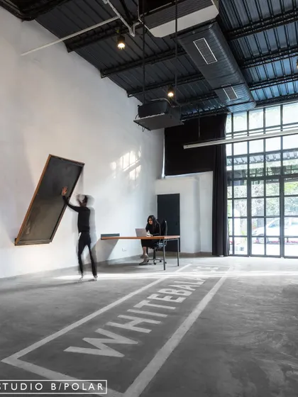 The main hall of the WhiteBalance office features polished concrete floors with the company logo stenciled on, preserving the raw, industrial aesthetic. The large, pivoting blackboard adds a functional and dynamic element to the space.