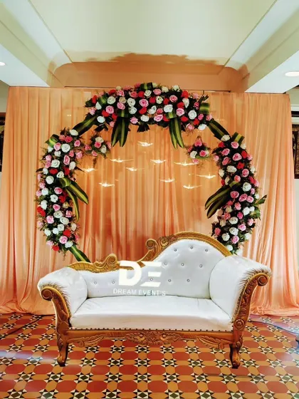 A circular floral arch in red and white creates a stunning focal point for this indoor event. The simple peach draping and patterned tile floor complement the arrangement, making it perfect for an engagement or reception.