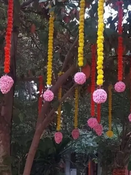 Decorative strings of marigold and pink flowers hanging from tree branches for an outdoor event.