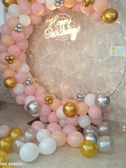 A charming birthday backdrop with a circular frame and a balloon garland in pink, white, and gold. The 'Happy Birthday' neon sign and fairy lights add a magical touch.
