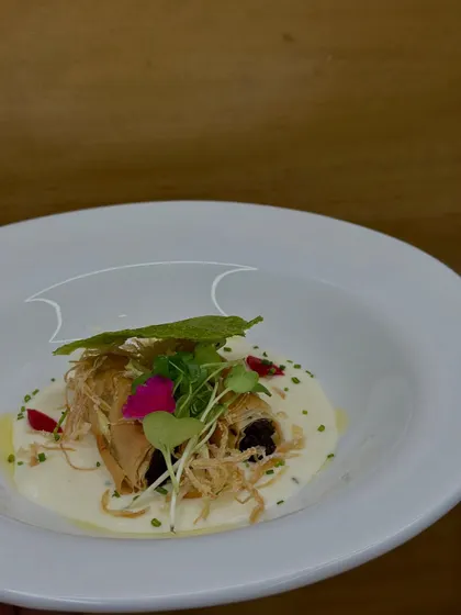 The third course, a beautifully plated Truffle Mushroom Éclair resting in a creamy parmesan sauce, garnished with microgreens and edible flowers.