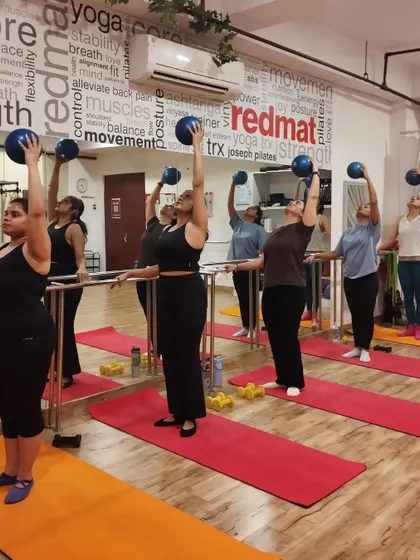 A group of women in a Barre class use small Pilates balls for an overhead press, adding an upper body challenge to their lower body work.
