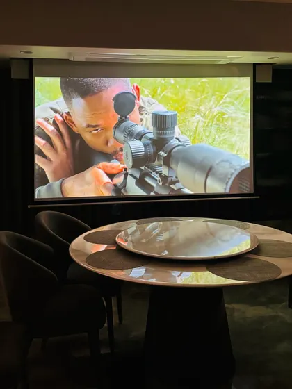 This setup shows how a projector can transform a dining area into an entertainment zone. The motorized screen drops down in front of the window, creating a perfect space for movie nights after dinner.