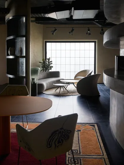 A moody and sophisticated seating area with a curved grey sofa and sculptural chairs. The large gridded window, although internal, mimics an external window, enhancing the 'mini-home' feel.