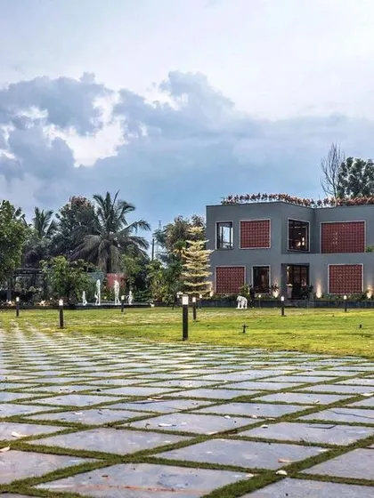 The grand approach to the farmhouse, with a gridded stone driveway leading the eye towards the main structure, set within a lush, green landscape.