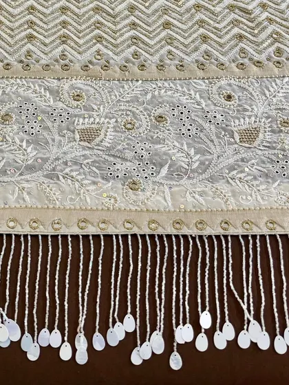 A close-up of the saree's pallu, featuring a dense chevron pattern and floral motifs, all highlighted with mirrorwork and finished with hand-sewn tassels.