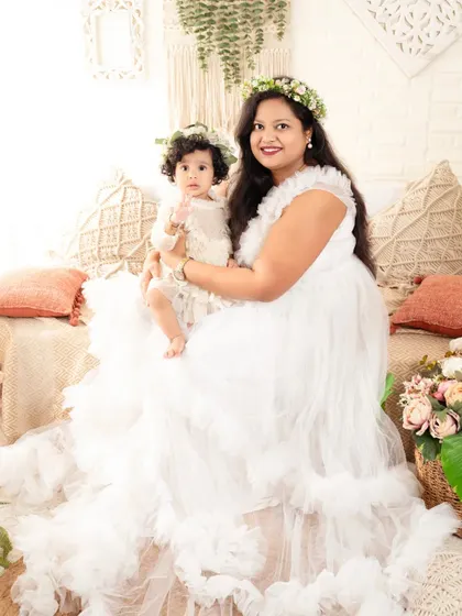 A beautiful mother-daughter portrait, both looking angelic in white dresses and floral crowns.