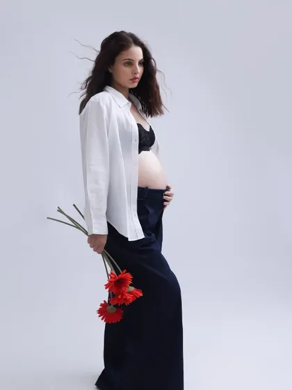 A striking and editorial-style portrait. The simple white shirt, dark trousers, and bold red flowers create a modern, artistic image that is both strong and feminine.