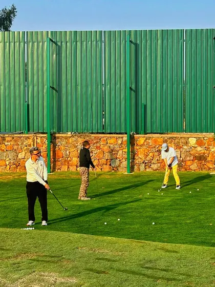 Three golfers work on their short game on the putting and chipping green.