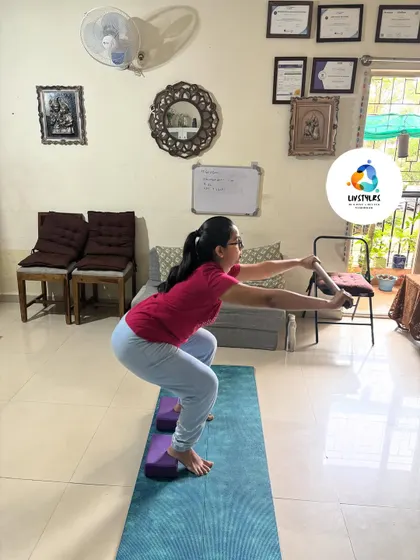 This client is using yoga blocks under her heels to achieve better depth and alignment in a squat. This modification is excellent for those with tight ankles and helps build proper form.