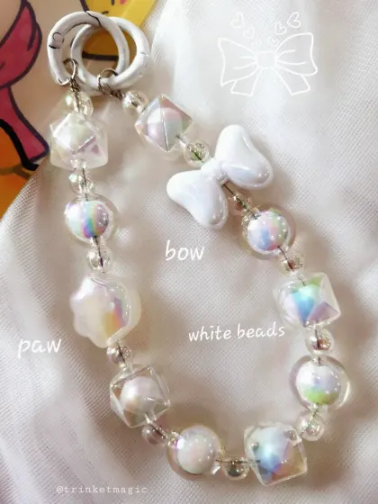 For the lovers of a clean, white aesthetic. This charm is made with iridescent white beads, a white bow, and a paw charm, making it a perfect gift for dog lovers.