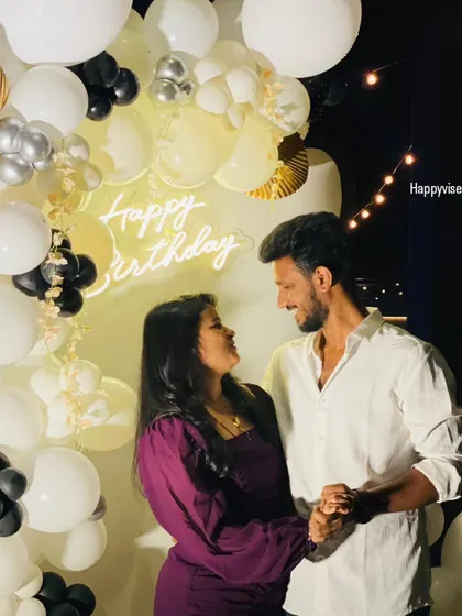 A candid moment from a surprise birthday party. The black, white, and gold balloon backdrop with a neon sign creates the perfect setting for making memories.