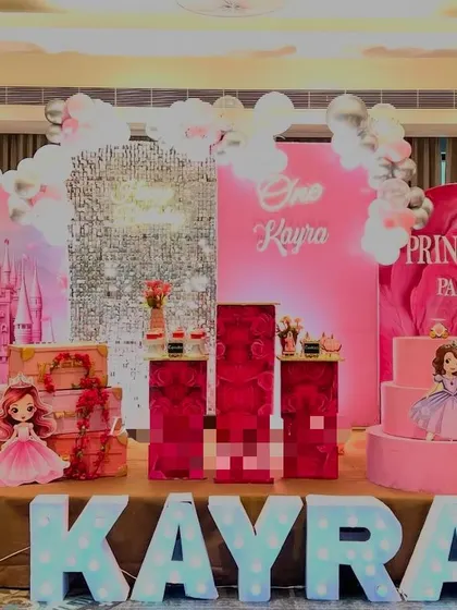 A pink-drenched Princess party for Kayra. The stage includes a castle backdrop, a silver shimmer wall, and a dessert table with a princess cake.