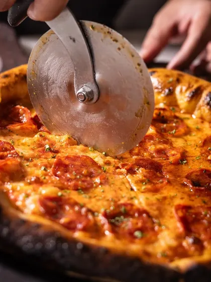A close-up of a pizza cutter slicing through a hot pepperoni pizza. It's a satisfying image that anticipates the enjoyment of sharing a meal.