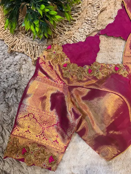 A close-up of a magenta silk blouse with gold zari border and floral embroidery, highlighting the rich texture of the fabric.