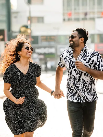 A joyful shot of the couple running and laughing on a sunlit city street.