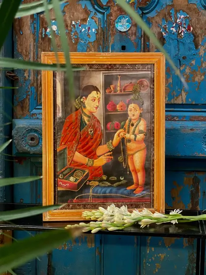 The Yashoda and Krishna cloth oleograph, seen through foliage. This handcrafted piece, with its three-dimensional embroidery, adds a unique and personal touch to any home.