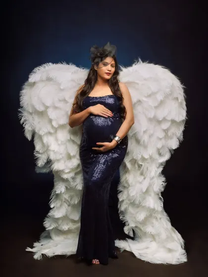 A truly angelic portrait featuring a mom-to-be in a sparkling blue gown, adorned with a magnificent pair of white feathered wings.