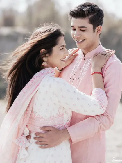Love and laughter captured in a candid embrace. The wind blowing through her hair adds a touch of natural movement to this happy moment between the couple in their lovely pink and white outfits.