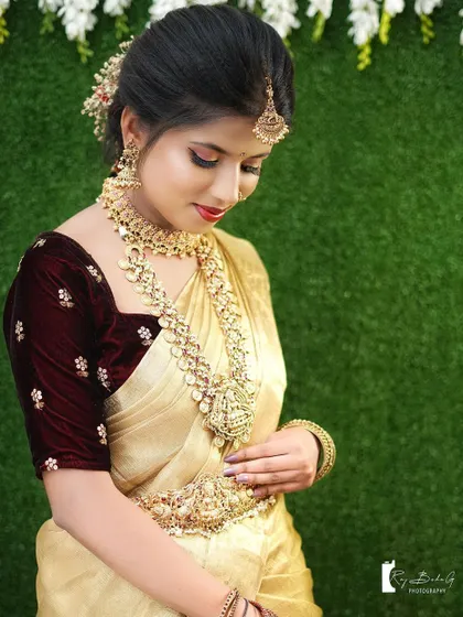 A serene portrait from a bridal photoshoot. The bride's makeup is classic and elegant, with a bold red lip and soft gold tones.