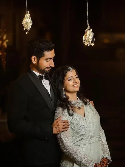 A romantic shot of the couple under hanging lights. Her soft glam makeup and wavy hair create a timeless and sophisticated reception look.