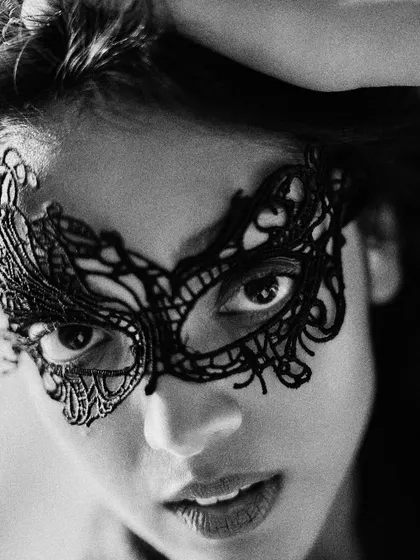 A black and white beauty editorial focused on mystery and allure. This close-up shot highlights a delicate black lace mask, drawing all the attention to the eyes.