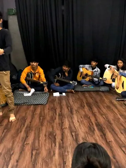 A full view of our guitar class, with the instructor at the whiteboard and students ready with their instruments. The vibrant mural in the background adds to the creative vibe.